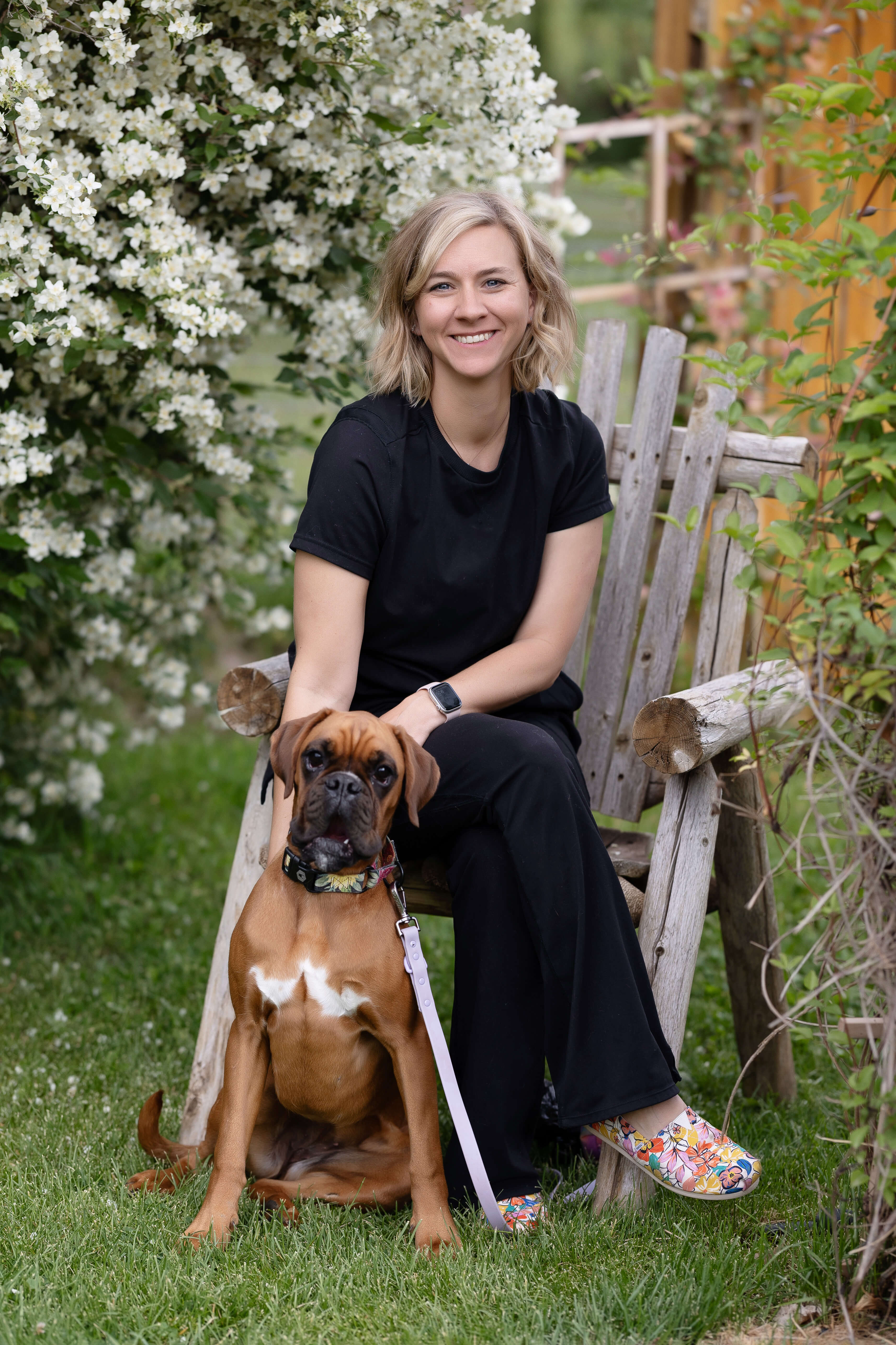 Woman in black scrubs with boxer puppy sitting in front of her.