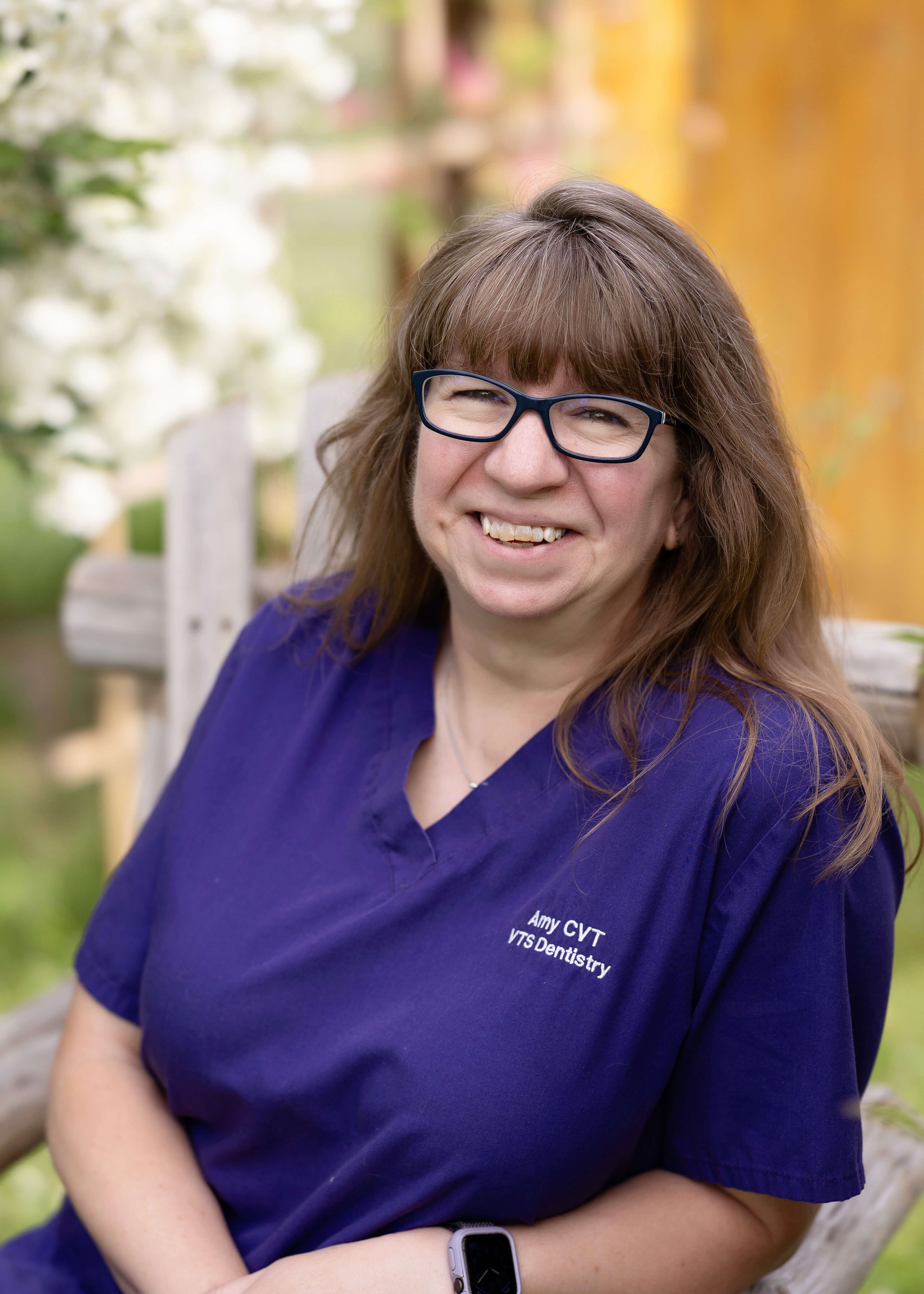 Woman with glasses, in purple scrubs sitting outside in a chair