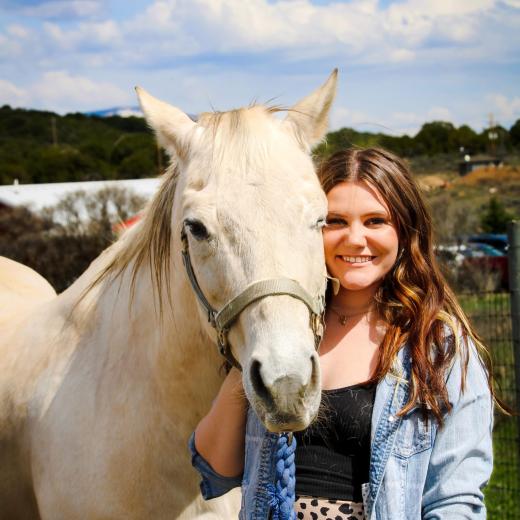 Young woman with long brown hair, standing next to a white horse.